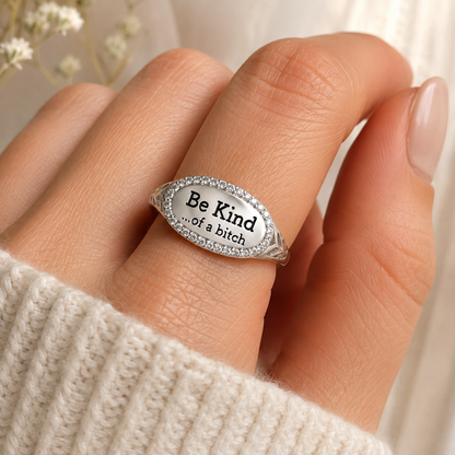 A silver oval ring with a pavé-set border and the engraved text 'Be Kind .