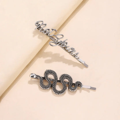 Two silver hair claw clips styled on a beige background. One clip features the word 'motivation' in cursive script, and the other is a coiled snake design with textured black and silver scales.