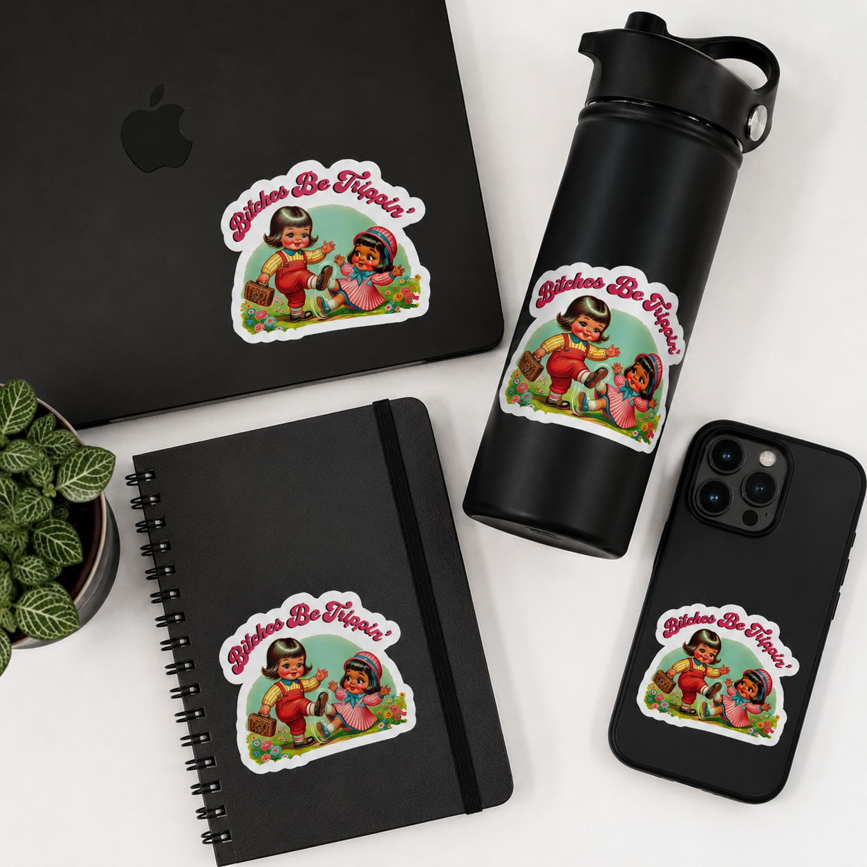 A set of black stationery and tech accessories featuring a matching die-cut sticker with a retro illustration of three children and the text 'Bitches Be Friends!'. The items include a laptop, notebook, water bottle, and phone case, arranged on a white surface with a small potted plant.