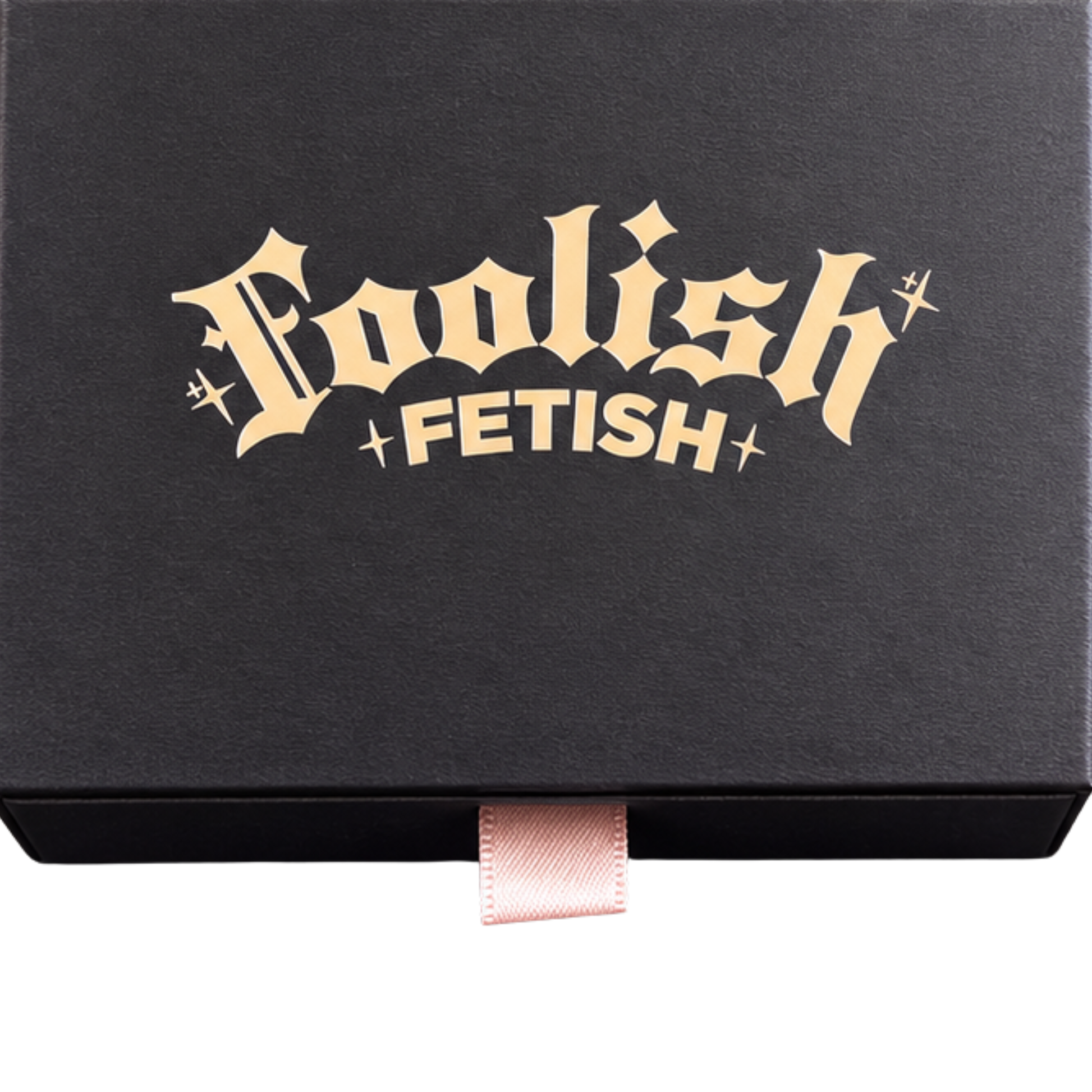 A black rectangular product box with the words 'Foolish Fetish' printed in a metallic gold gothic font on the lid, with a small pink ribbon pull tab at the bottom center, shown on a white background.