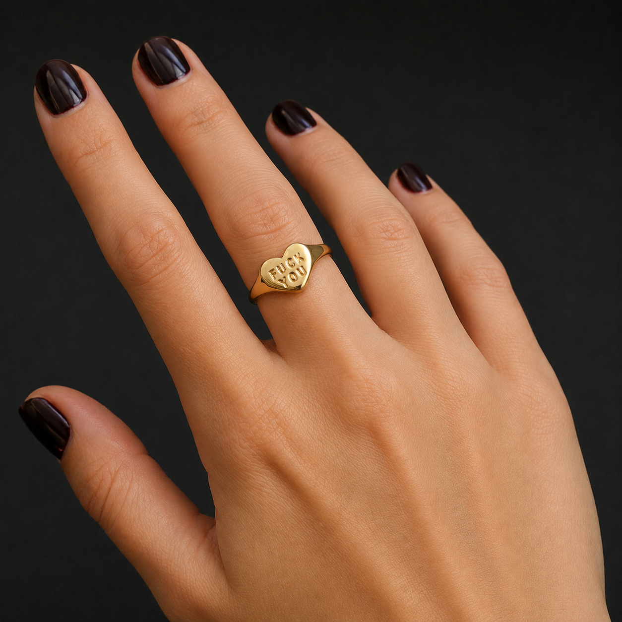 A close-up of a hand with dark manicured nails wearing a gold signet ring engraved with the initials 'B & B' on a dark background.
