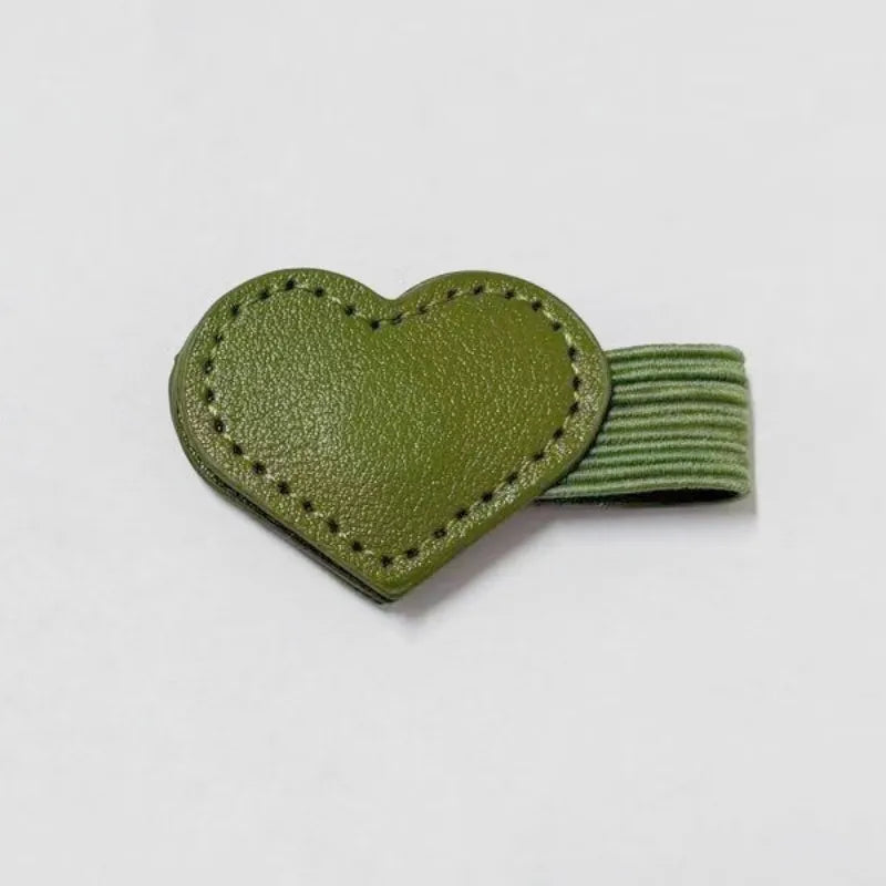An olive green heart-shaped leather keychain or bag charm with a matching ribbed elastic loop, shown on a plain light gray background.