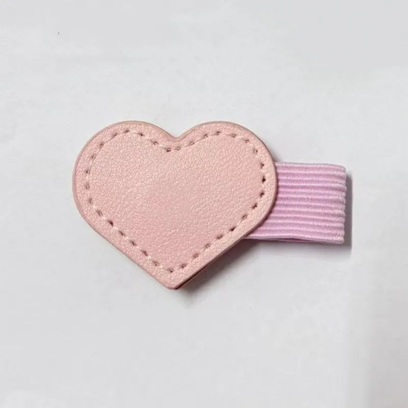 A light pink heart-shaped hair clip with a textured faux-leather front and a ribbed elastic band, shown on a plain light gray background.