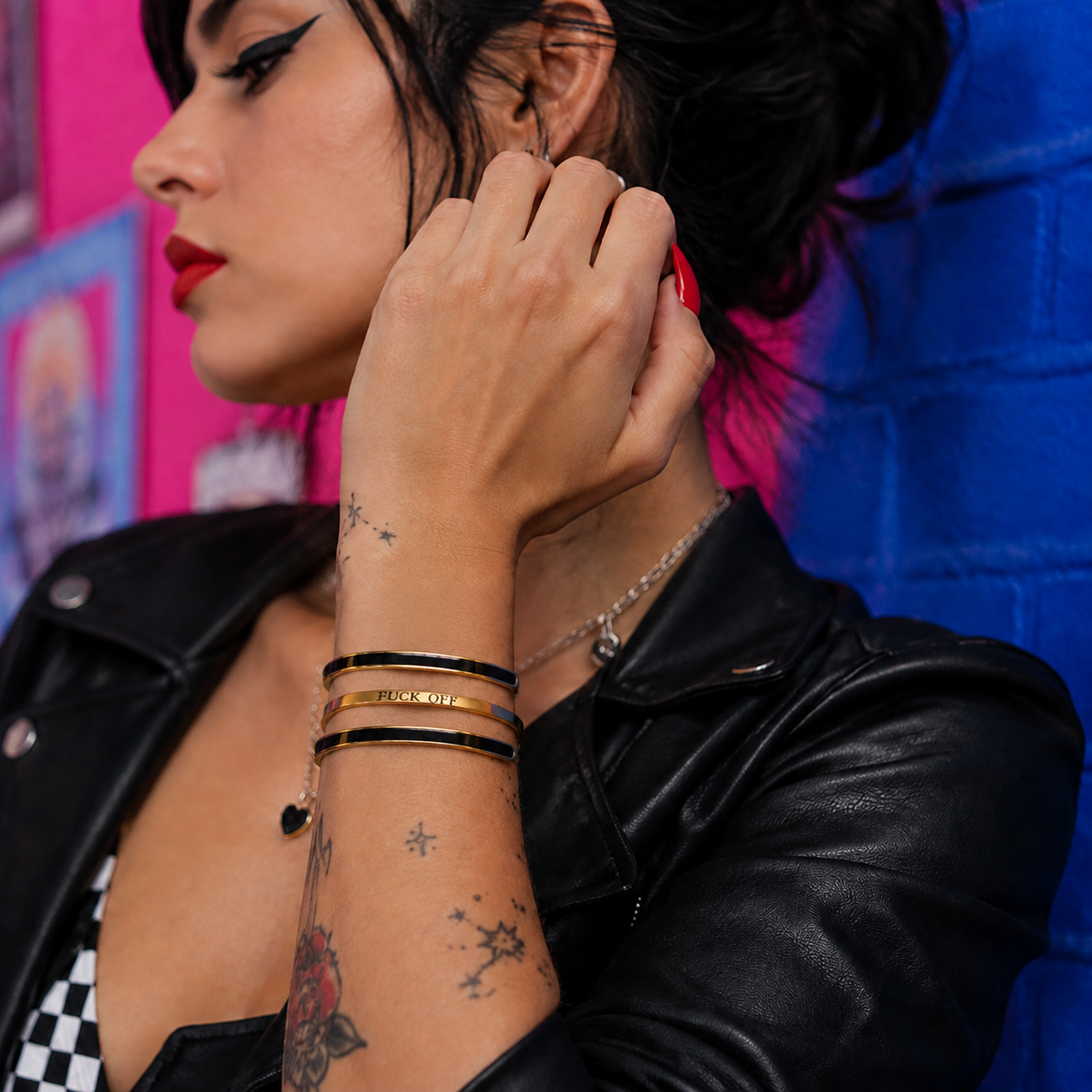 Three stacked black and gold cuff bracelets with a gold Fuck Off bracelet worn together
