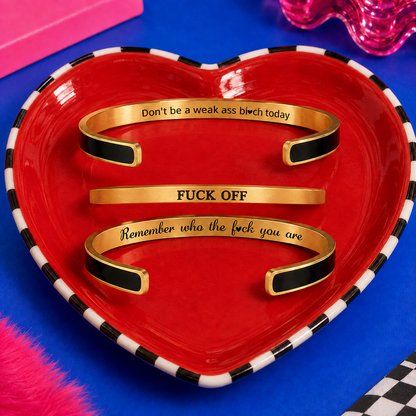 Two black and gold hidden message cuffs displayed with a slim gold Fuck Off bracelet