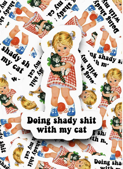 A die-cut sticker featuring a vintage-style illustration of a blonde girl in a red-and-white gingham dress holding a black-and-white cat, with the text 'Doing shady shit with my cat' on a white background. The sticker is shown layered over a repeating pattern of the same design.