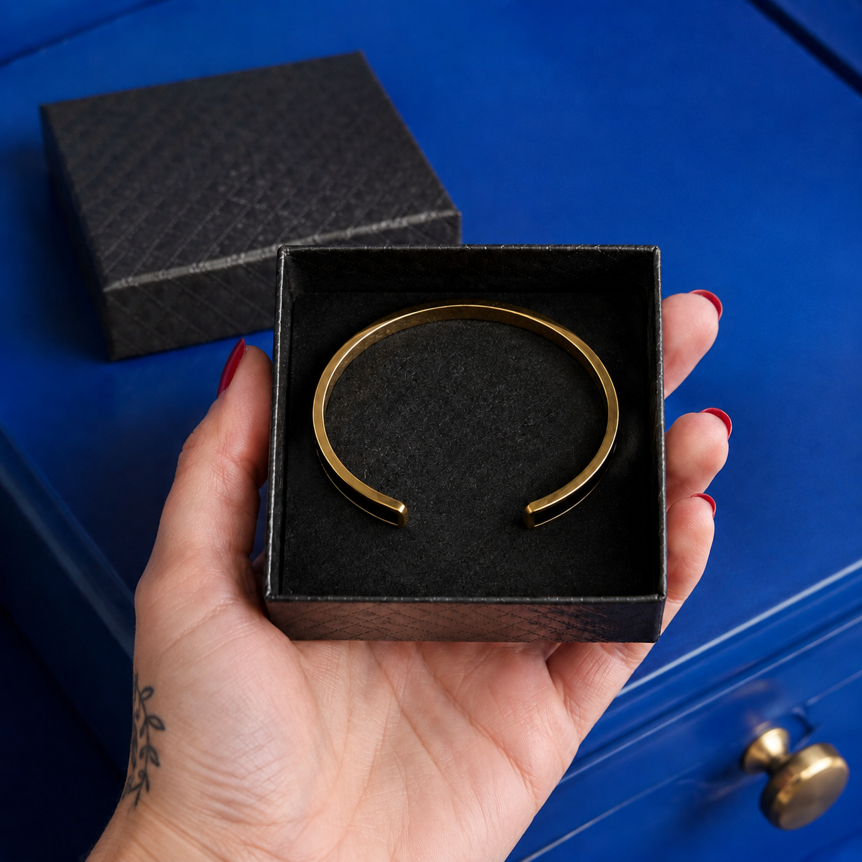 Gold cuff bracelet presented in an open black gift box held by hand