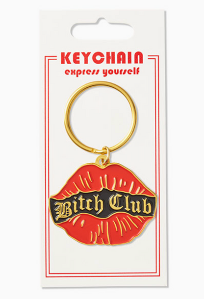A red lips-shaped keychain with a black center banner reading 'Bitch Club' in gold lettering, attached to a gold metal key ring and displayed on a white retail card.