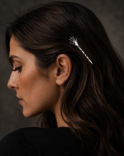 A woman in profile wearing a delicate silver hair claw clip tucked behind her ear, shown against a dark textured background.