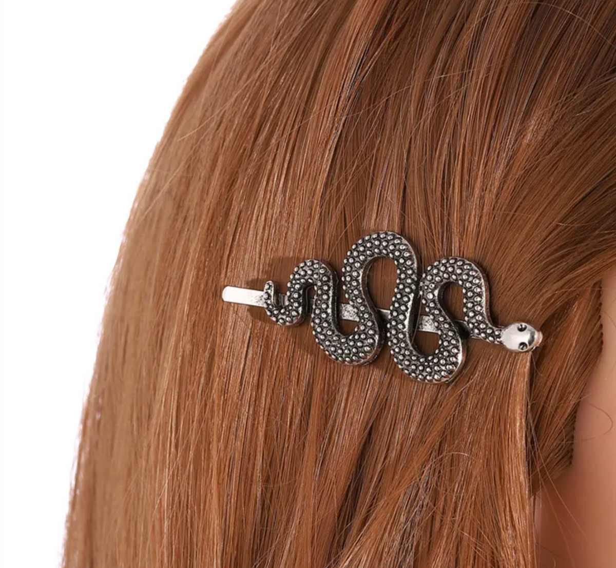 A silver snake-shaped hair claw clip with textured rhinestone detailing, shown clipped to the side of a model's auburn hair against a white background.