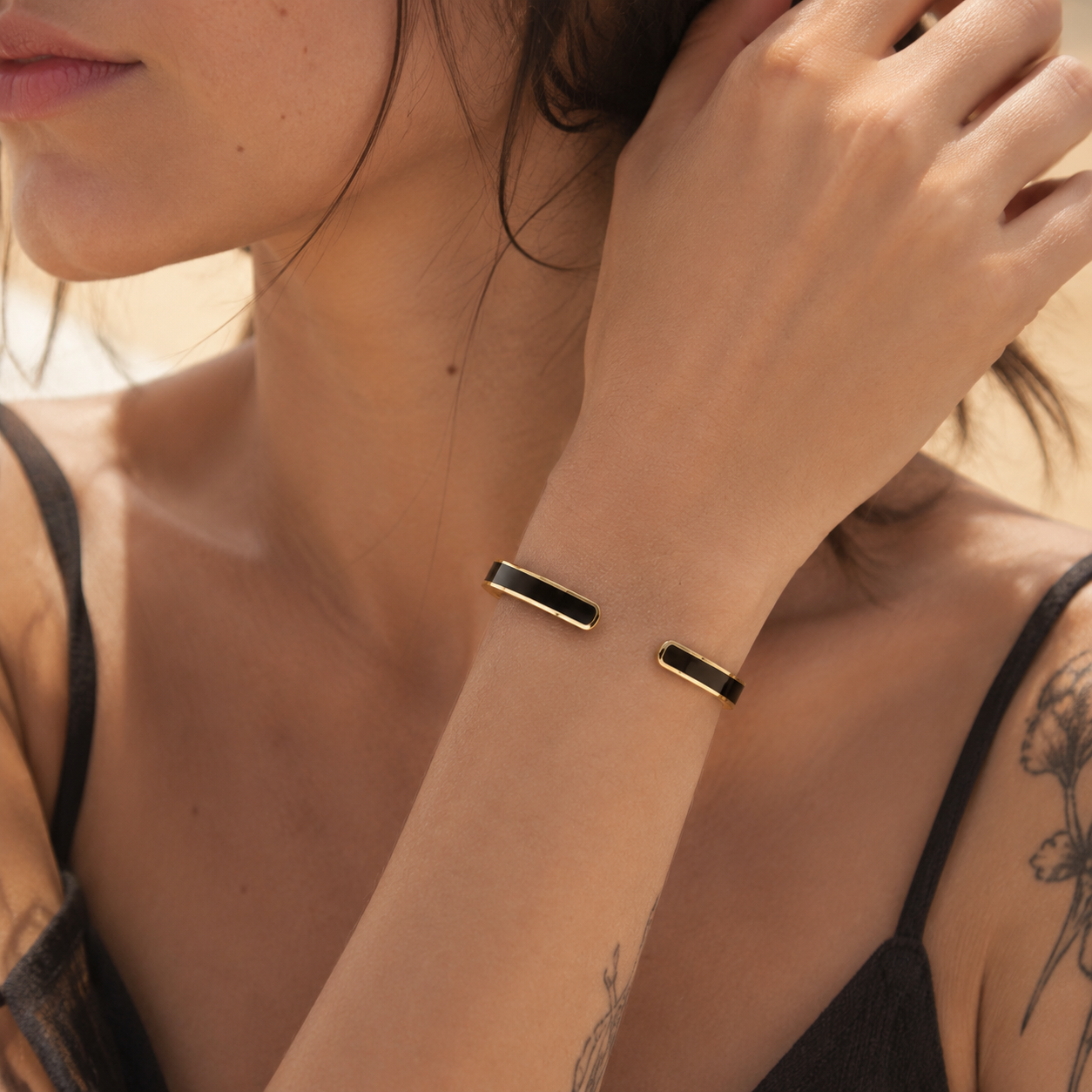 Slim black and gold open cuff bracelet worn on a woman's wrist