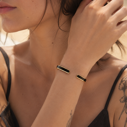 Slim black and gold open cuff bracelet worn on a woman's wrist