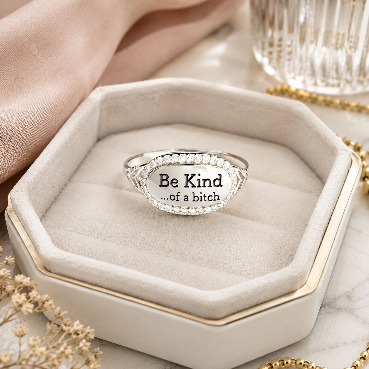 A silver oval ring with clear stones and the printed message 'Be Kind .