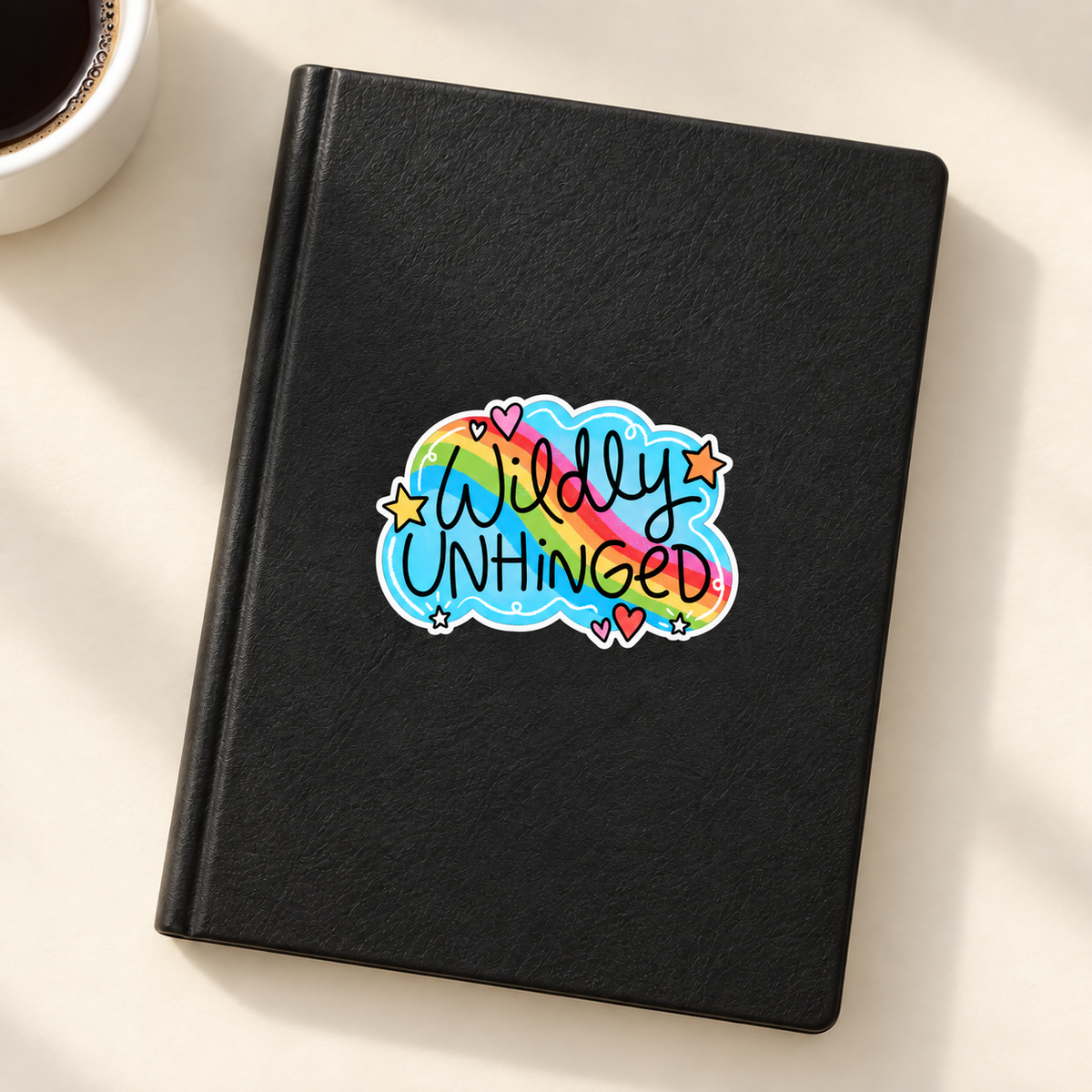 Wildly Unhinged rainbow sticker on black notebook