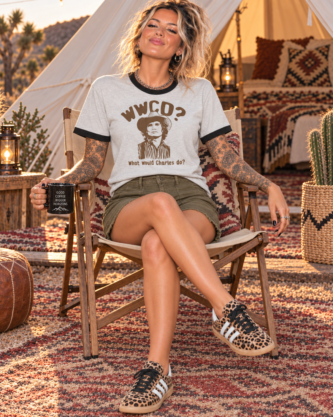 A woman sitting in a wooden camp chair wearing a light gray graphic t-shirt with black trim, olive green shorts, and leopard print sneakers in a rustic outdoor setting with a teepee tent and patterned rugs.